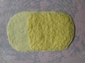 一发完成的面团倒在揉面垫上，用手按压排气后擀成长方形，然后将椰蓉馅料平铺在面团的2/3处，留1/3不铺馅料