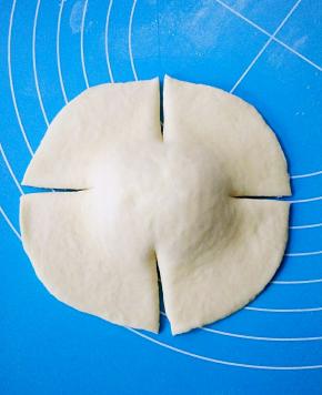 取一个面团底部朝上，用擀面杖擀成边缘薄，中间厚的圆片，用刮板在面团上下左右切4个口。