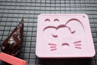 制作巧克力配件。用到KT慕斯圈套件中的硅胶模具，裱花带放入巧克力隔热水融化后，挤入到模具中，抹平。冷藏一会即可，用的时候脱模。