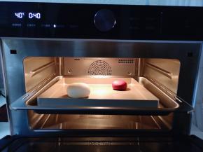 把和好的面团从面包机里取出后揉圆，把两块面团放入美的蒸烤箱进行发酵。（将蒸烤箱水盒取出，加满纯净水，再将水盒放入机体推回原位）