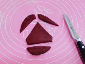 开始做圣诞老人帽子、取一块红色面团揉匀擀成椭圆形薄面片、用刀把多余的部分切掉。如图！