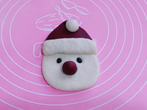 把做好的白色小圆球放在帽子顶部、取一点红色面团做一个小圆球装饰圣诞老人的鼻子、两颗黑豆做眼睛！如图