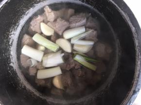 将去掉血水的牛肉连汤汁一起倒入高压锅内，加入葱段跟蒜，高压锅压软