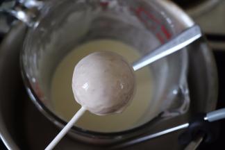 白巧克力放入容器中，隔热水融化成液态。温度不可过高。棒棒糖棍沾一下巧克力，插到蛋糕中，在巧克力中滚一滚。最好插在泡沫板上，晾到凝固。