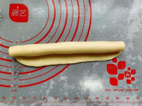 取一个松弛好的小面团，用擀面棍擀成牛舌状，翻面后将长的一边的底边擀薄，从上往下卷成长条状，收口捏紧。