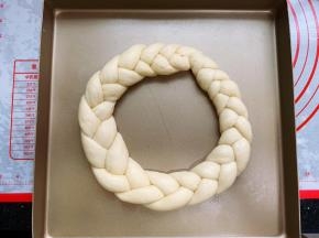 将编好的辫子围成一个圆圈，首尾相连，收口捏紧，另外三条也是同样的方法。然后放在不沾烤盘里，一个烤盘放一个辫子花环面包胚，分两次烘烤。