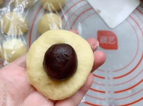 取一个醒发好的面团用手将其拍扁，包入豆沙馅。