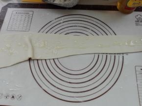 用擀面杖将其擀成一端窄一端宽的面片，同时在面片上面抹上适量食用油，涂抹均匀