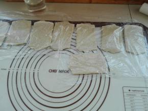 将折叠三折后的面团，对折面朝下放置，同样用擀面杖将其最后再擀长一下，依次全部做好，盖好保鲜膜醒发10分钟，如图所示。