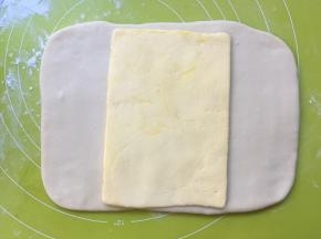 揉面垫上撒点干粉，冰箱取出冷冻的白色面团，冰箱取出冷冻的黄油片，用刀裁开保鲜袋，将黄油片放在面片中间 
