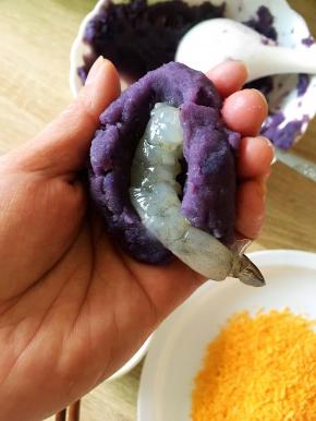 将土豆泥均分成约7份，搓圆压扁后放入鲜虾包裹好，只留尾巴露出。