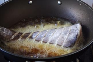 当油六、七成热时放入鱼，此时改中火。 
煎鱼时随时微微调整火的大小，千万不要让油起烟。 
六、七成热的油温是如何判断呢，就是油面有明显的波动。 往油锅里放鱼时，用双手分别拎住鱼头和鱼尾，贴着油面轻轻地放入。
我使用的是不粘锅。 如果小伙伴们使用的是铁锅就要把锅烧的热热的，然后用姜在锅里涂抹一层，再继续操作。