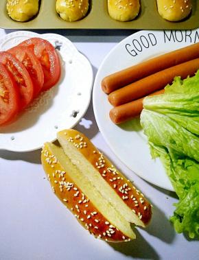 准备好蔬菜和煎好的香肠，用锯齿刀从面包中间切一刀底部不切断。
