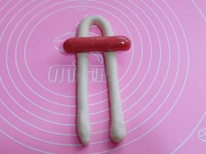 取一块醒发好的面团，搓成长条状，每条约40厘米左右！再将长条对称弯过来，将香肠放在上面，如图！