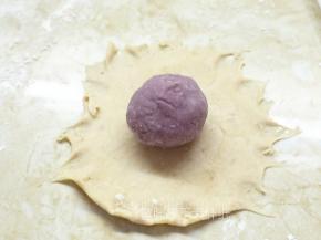 取一个松弛好的面团，用擀面杖自中间向四周擀开，成圆状。在面团的中间放上一个紫薯芋泥馅。