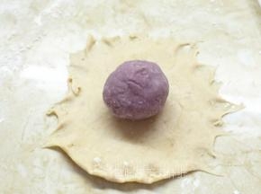 取一个松弛好的面团，用擀面杖自中间向四周擀开，成圆状。在面团的中间放上一个紫薯芋泥馅。
