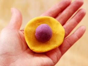 用手摁扁后，把静置好的紫薯揉成圆球放到南瓜面皮上面。