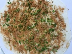 案板上撒少许面粉，面团用擀面杖擀成薄片。用手均匀地涂抹一层自制椒盐。用铲子把猪油均匀的涂抹在面片上。均匀的撒上孜然粉，猪油渣末儿，葱花。