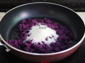 捣碎的紫薯泥倒入平底锅，然后放入白砂糖，炒至白砂糖溶解，然后加入玉米油，中小火翻炒，让紫薯泥完全吸收油，变干能揉搓成团不散即可出锅。