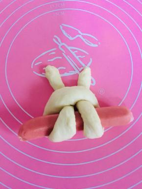 面团的一头绕过烤肠，从半圆穿过去。两边都穿过去，整理一下面团，小兔子初见雏形了。