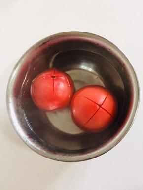 西红柿顶部用刀划十字刀，放在容器中，倒入开水烫一分钟左右。