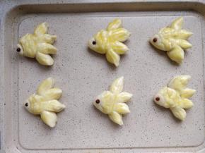 将做好的小鱼放到不粘烤盘上，用红豆充当眼睛，再用裱花嘴的圆形或者金属勺子头在鱼身上按出弧形鱼鳞的图案。将少许蛋黄液加水调匀，刷在表面。