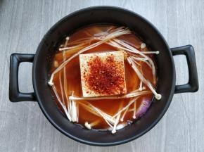 将北豆腐放入汤盅里，洋葱切条，金针菇撕成细条，都放在豆腐周围。第一步调好的汤汁倒入汤盅里。