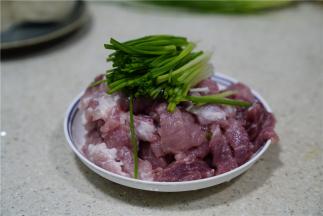 将猪肉改刀，然后加入葱段。
