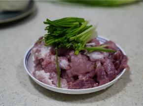 将猪肉改刀，然后加入葱段。