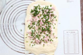 再把火腿碎和葱花均匀的铺在面团上面，但要注意最底部不用铺，因为等会卷起时，才能更好的沾住