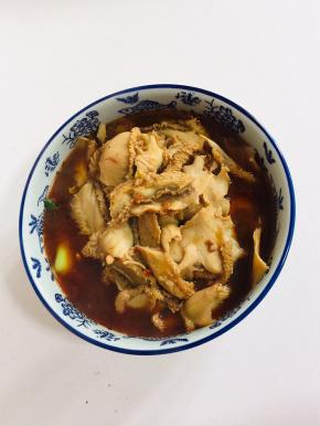 把煮好的牛肚倒在碗里的配菜上。