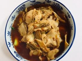 把煮好的牛肚倒在碗里的配菜上。