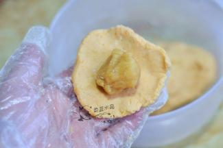 取一块面团揉圆压扁，放入馅料包起来，稍微按扁。