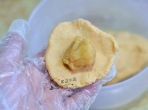 取一块面团揉圆压扁，放入馅料包起来，稍微按扁。