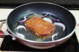 用大火调制高温，放入腌制好的牛排，洋葱。牛排煎至表面的颜色为深褐色，散发出香味，翻转另外一面继续煎至深褐色。这个时候改为小火，继续煎，每30秒翻转一次，煎至有弹性，七成熟即可。