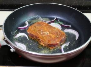 用大火调制高温，放入腌制好的牛排，洋葱。牛排煎至表面的颜色为深褐色，散发出香味，翻转另外一面继续煎至深褐色。这个时候改为小火，继续煎，每30秒翻转一次，煎至有弹性，七成熟即可。