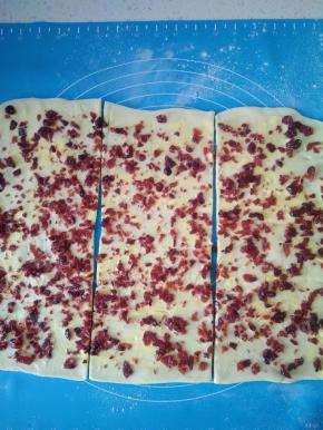 取出冷冻的面团，用擀面杖擀成长方形薄片，在表面均匀地抹上软化黄油，撒上切碎的蔓越莓干。