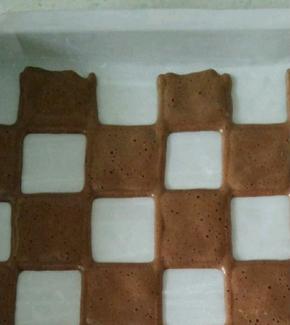 在描有黑点的方格里填充可可蛋糕糊，抽出图案纸，放入预热好的烤箱150度2分钟。