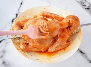 把煮沸的蜜汁腌料先在三黄鸡全身涂抹一遍，不要全涂完，留下一点，因等下还要再刷一遍，这样能让鸡烤出来颜色更漂亮