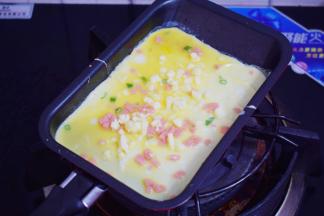 迷你煎锅小火烧热，舀进1大勺鸡蛋液，再撒上芝士碎，小火煎至底部凝固