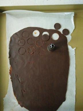 用少量巧克力在油纸上挤上眼睛和鼻子，剩余巧克力倒在铺好油纸的烤盘上，表面再铺张油纸擀平待凝固，用热的裱花嘴刻出小熊耳朵。