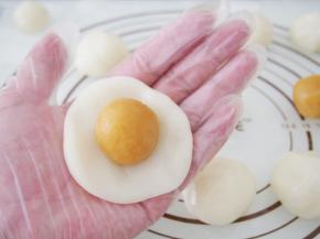 取一块冰皮面团轻轻压扁，将奶黄馅放上，用虎口轻轻收起来。