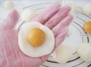 取一块冰皮面团轻轻压扁，将奶黄馅放上，用虎口轻轻收起来。