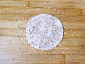 案板上撒一层白芝麻，然后拿起刷了蜂蜜水的面皮，在芝麻上面压一下，让面皮两面都沾满芝麻。