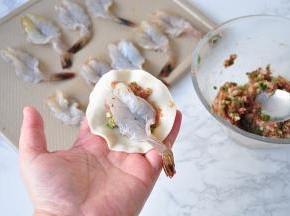 取一个饺子皮，放在适量肉馅，然后放入一个虾。