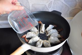 开火，将饺子的底壳煎至上色，微微黄的状态，加入水，没到饼子二分之一处即可。盖上锅盖大火烧开后转中火。