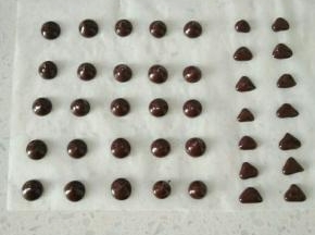 15巧克力币隔水融化，在油纸上挤出大小一致的圆片，装饰小熊眼和鼻子。
