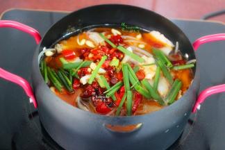 把煸炒好剩余的三分之一的辣椒、以及辣椒油、香葱等倒入煮好的鱼盆里。