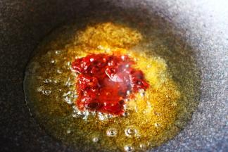 锅中倒入花生油烧热后放入郫县豆瓣酱进行煸炒。