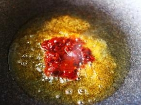 锅中倒入花生油烧热后放入郫县豆瓣酱进行煸炒。